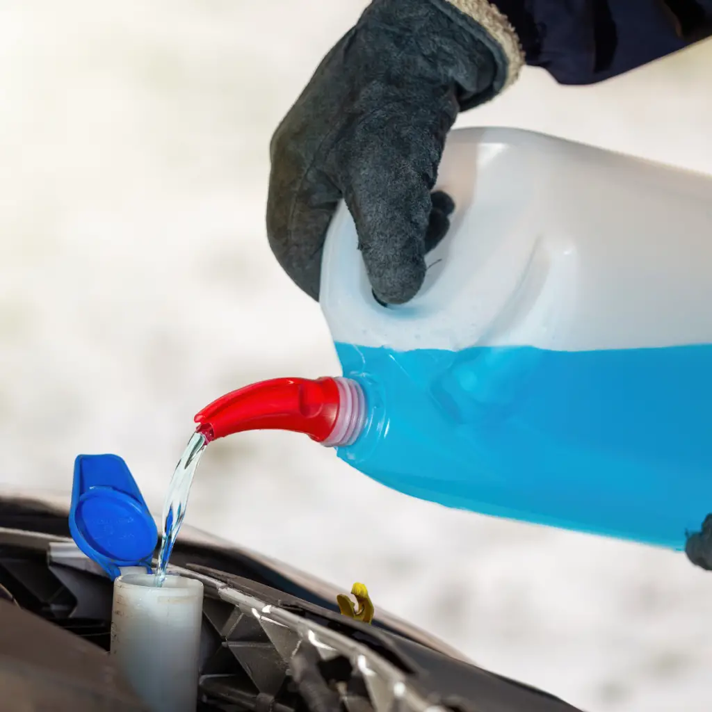 Person pouring antifreeze coolant into a car reservoir